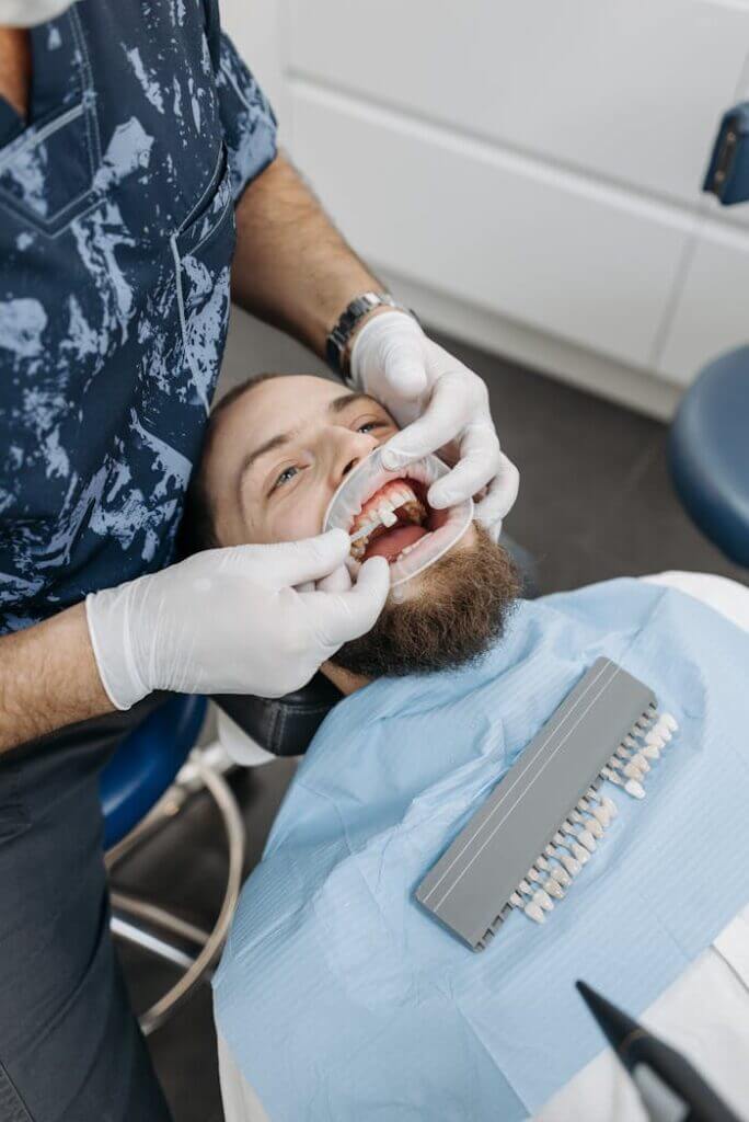 patient-at-the-dentist-6812534 A dentist examines a patients teeth using dental tools in a clinic setting.